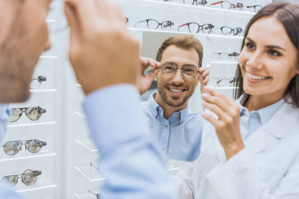 istock cheerful female optometrist holding mirror while smiling man choosing eyeglasses in ophthalmic shop 1053517280
