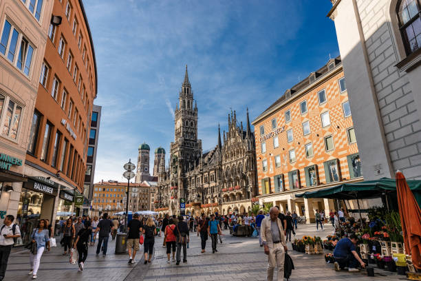Munich, Germany - September 6th, 2018: Marienplatz, is the most important town square of Munich and is a pedestrian zone. On background the New Town Hall (Neue Rathaus) XIX century in neo-Gothic style, and the two bell towers of the cathedral. Tourists and locals stroll around the square and shop in the many shops. Bavaria, Germany, Europe.