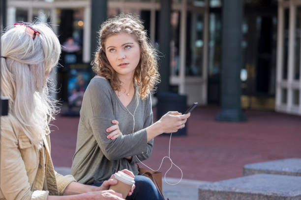 Teenage girl ignores her grandmother Rude teenage girl rolls her eyes at her grandmother. The girl is listening to music on her smartphone. She is wearing earbuds. rolling eyes stock pictures, royalty-free photos & images