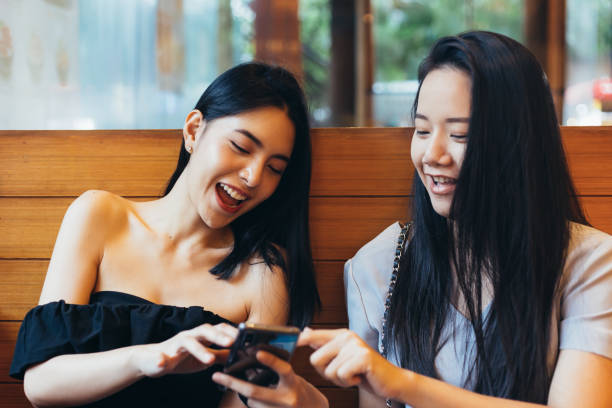 istock Two young attractive Asian women using a mobile phone together at restaurant with happiness and joy 1053525866