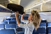 Young woman places luggage in airline overhead bin