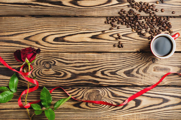 полная чашка черного кофе возле одной красной розы и разбросанных кофейных зерен и подарок и красная лента на старом деревянном столе. вид � - coffee bean coffee flower ribbon стоковые фото и изображения