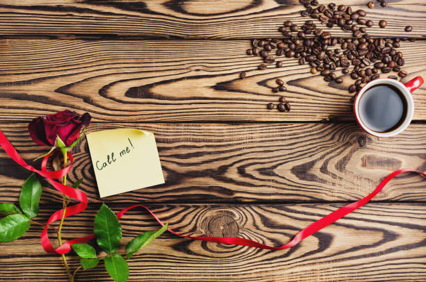 anmeldung rufen sie mich an papier neben rote rose mit band und eine tasse kaffee in der nähe von kaffeebohnen auf alten holztisch. draufsicht mit textfreiraum. sankt valentin-tag-konzept - coffee bean coffee flower ribbon stock-fotos und bilder