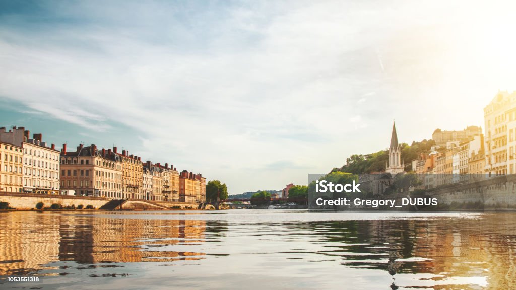 Beautiful sunset over Lyon city buildings with St Georges church on right in France seen from Saone river point of view Color photography of Lyon city buildings, french culture architecture and wonderful ancient monuments in France, in Rhone, Auvergne-Rhone-Alpes region, seen from a boat on Saone river point of view in summer. Image taken from public area outdoors, along riverbank. Lyon Stock Photo