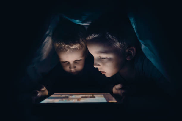 dwoje dzieci z tabletem w ciemnym pokoju - hiding internet multimedia people zdjęcia i obrazy z banku zdjęć