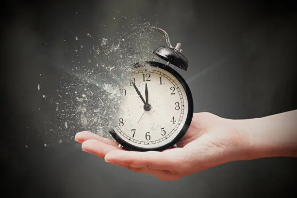 Concept of passing away, the clock breaks down into pieces. Hand holding analog clock with dispersion effect