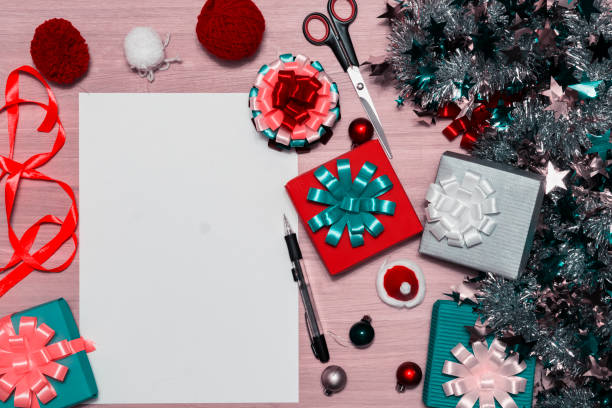 istock Gift boxes. on wooden table. Christmas tinsel and multi-colored bows. In the center is a white sheet with a fountain pen. 1053557864
