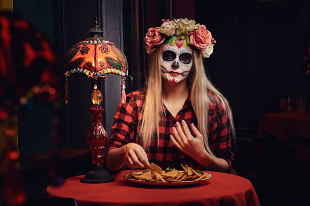 멕시코 레스토랑에서 나 초를 먹는 꽃 화 환에서 언 데드 화장과 젊은 금발 소녀. - day of the dead mexico bride human skeleton 뉴스 사진 이미지