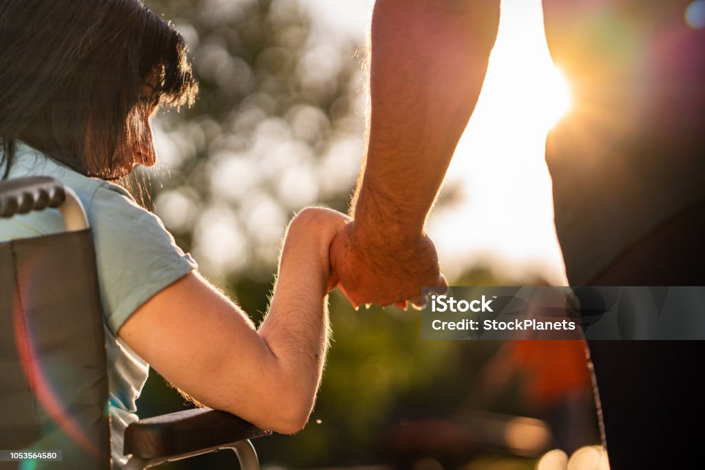 Couple hands during sunset Close up women on a wheel chair holding mens hand Disability Stock Photo