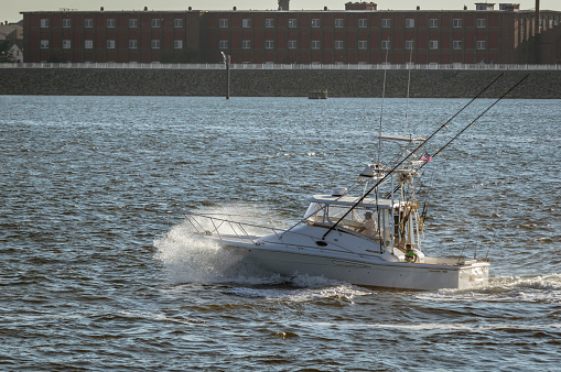 New Bedford, Massachusetts, USA - September 5, 2018: Sport fishing boat Wild Horses crashing through evening chop in New Bedford outer harbor with mill in background