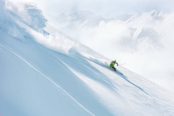 Man skiing down a steep slope on fresh snow stock photo