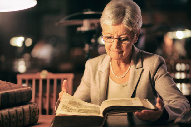 istock Senior woman reading in library at night 1053569518