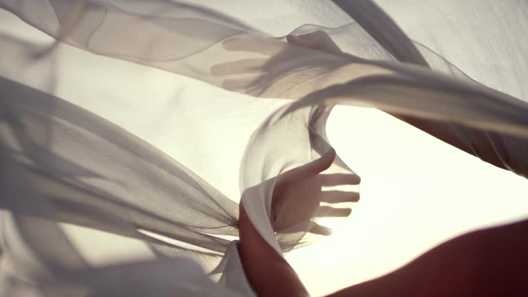 Junge Frau im langen Sommerkleid, die im Wind fliegt und an einem felsigen Ufer steht