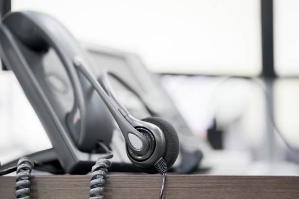 istock close up focus on call center headset device at VOIP system set up on telephone machine and monitoring computer at office desk for hotline telemarketing and network operation concept 1053578508