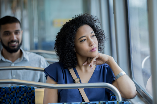 Serious young woman gazes out train car window while using public transportation to reach her destination. Young commuters are riding train.