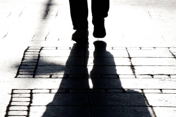 Silhouette shadows of a person legs walking on city street sidewalk stock photo