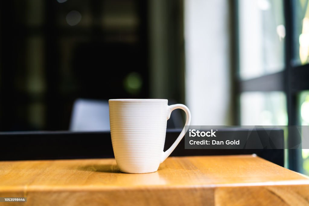 Blanco taza de café o té en una mesa de madera en una oficina o espacio de coworking - Foto de stock de Mesa - Mueble libre de derechos