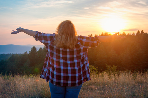 Overweight woman looking at the sunset with arms outstretched