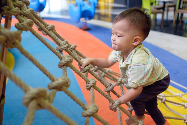 かわいい小さなアジア 2 歳幼児赤ちゃん男の子の子供楽しい屋内遊び場でジャングルジムに登るしようとすると、 - 子供　挑戦 ストックフォトと画像