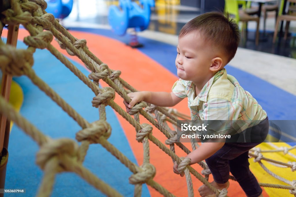 Cute little Asian 2 years old toddler baby boy child having fun trying to climb on jungle gym at indoor playground Cute little Asian 2 years old toddler baby boy child having fun trying to climb on jungle gym at indoor playground, Physical, Hand and Eye Coordination, Sensory, Motor Skills development concept Child Stock Photo