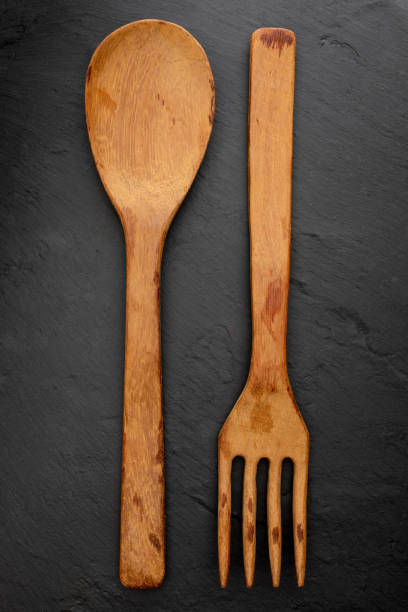 istock Wooden spoon and fork on textured black chalkboard background. Space to insert your text here. Letter for restaurants. (Food concept of spoon, pot). 1053611590