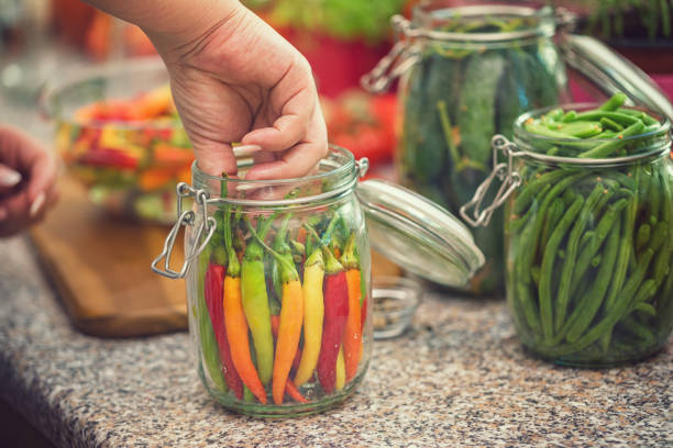 Young women preserving fresh organic chili peppers in jars at home