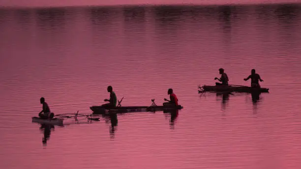 Photo of SILHOUETTE Unrecognizable local fishermen fishing in small boats at pink sunrise