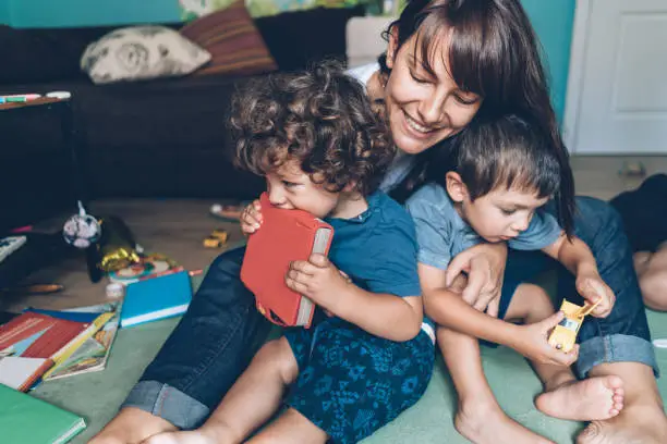 Mother hugging and playing with her little sons on the floor