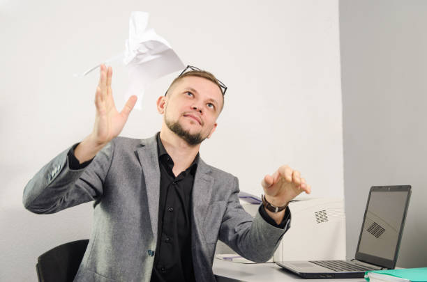 istock man in jacket throws up crumpled documents at table with laptop and printer in office 1053718206
