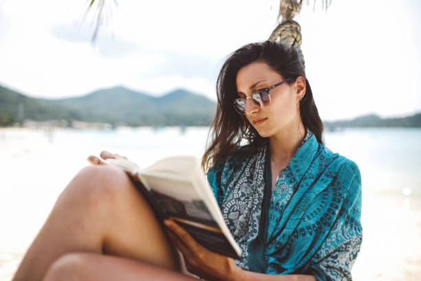 istock Young woman reading on the beautiful Koh Phangan sandy beach 1053720594