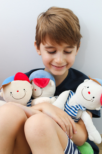 Little boy holding three cute boy cloth doll, front view