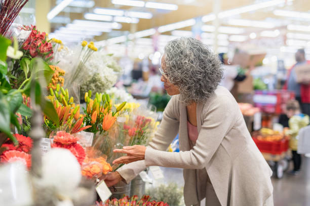 年配の女性が店で花をピックアップします。 - florist supermarket flower bouquet ストックフォトと画像