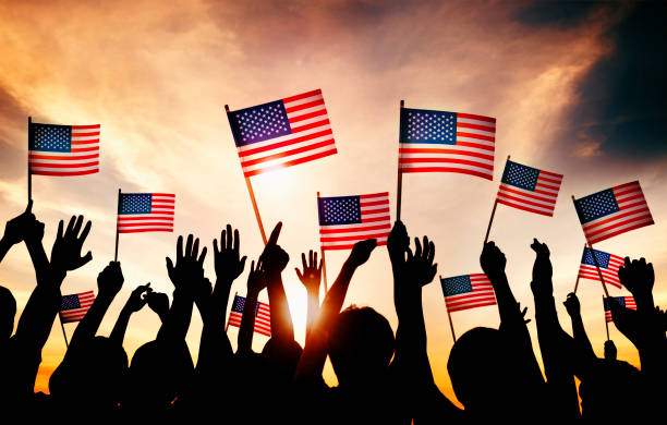 group of people waving american flags in back lit - american flag flag usa sky imagens e fotografias de stock