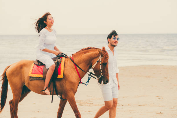 istock Young couple goes horse riding on tropical beach. 1053748762
