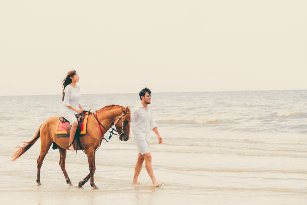 istock Young couple goes horse riding on tropical beach. 1053748802