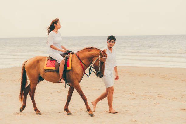 istock Young couple goes horse riding on tropical beach. 1053748838