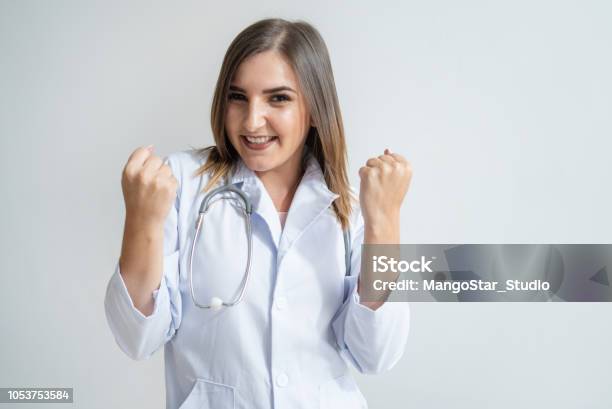 Positiven Kaukasischen Frau Im Kittel Zeigt Erfolg Geste Mit Geballten Fäusten Porträt Von Ziemlich Dunkelhaarige Junge Ärztin Die Lächelnd Auf Sie Recoverykonzept Stockfoto und mehr Bilder von Arzt