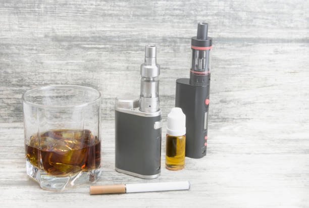 istock Whiskey in a glass with an e-cigarette and liquid for it on a gray stone background 1053755704