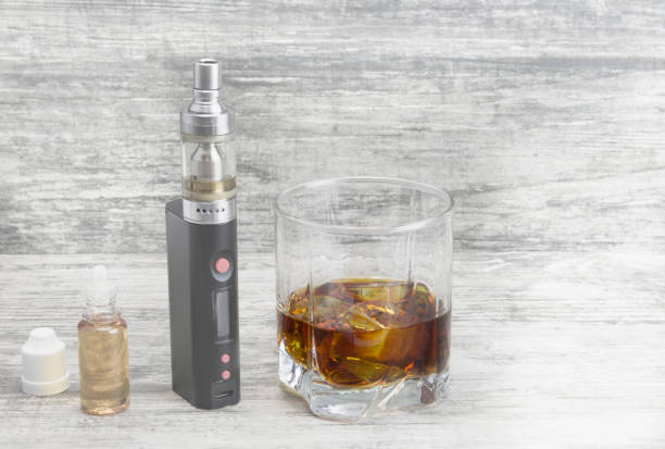 istock Whiskey in a glass with an e-cigarette and liquid for it on a gray stone background 1053755714