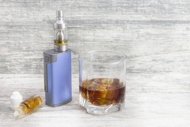 istock Whiskey in a glass with an e-cigarette and liquid for it on a gray stone background 1053755722