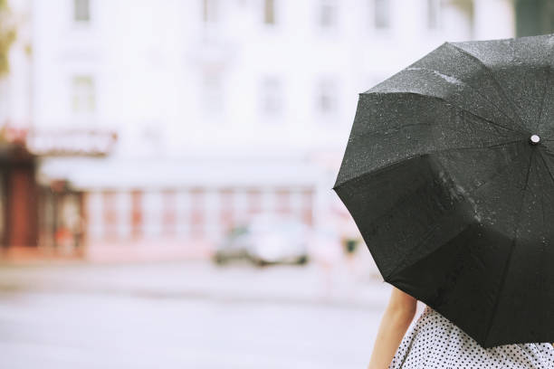 湿気のある天候。秋の雨。水玉ドレスを着た女の子は、黒い傘を保持します。街で雨が降っています。通りの背景にぬれた傘は。女性は、雨の中で逮捕されました。うつ病で一人の少女 - wet dress rain clothing ストックフォトと画像