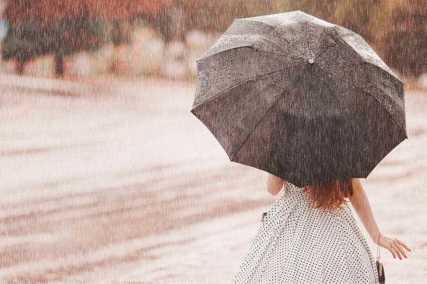 湿気のある天候。秋の雨。水玉ドレスの落ち込んでいる女の子は、黒い傘を保持します。市では雨が降っています。通りの背景にぬれた傘は。女性は、雨の中で逮捕されました。一人で落ち� - wet dress rain clothing ストックフォトと画像