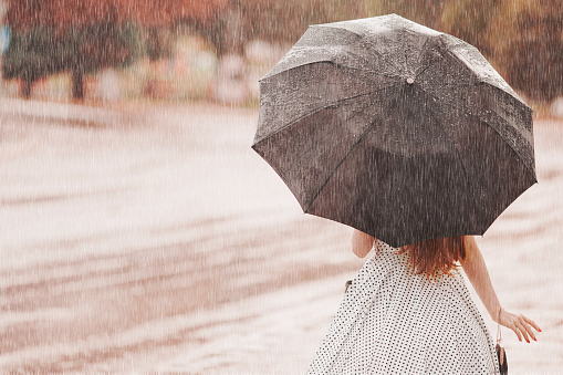 Wet weather. Autumn rain. Depressed girl in polka dots dress hold  black umbrella. Raining in city. Wet umbrella against the backdrop of the street. Woman was caught in the rain. Alone depressed girl