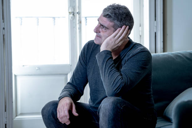 istock Attractive man feeling desperate sad looking worried depressed thoughtful and lonely suffering depression on couch at home in middle age crisis mental health personal problems and life style concept. 1053795962