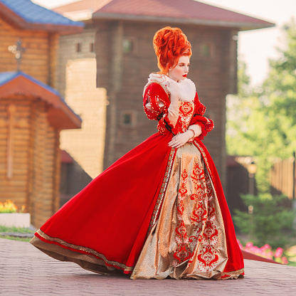 Fairytale countess in castle. Young baroque redhead queen with historical hairsdo. Renaissance princess with red hair. Fairytale queen in red gown with collar. Baroque countess with rococo hairdo