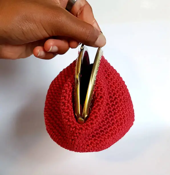 fingers of a young girl open her small purse in red knitted cotton