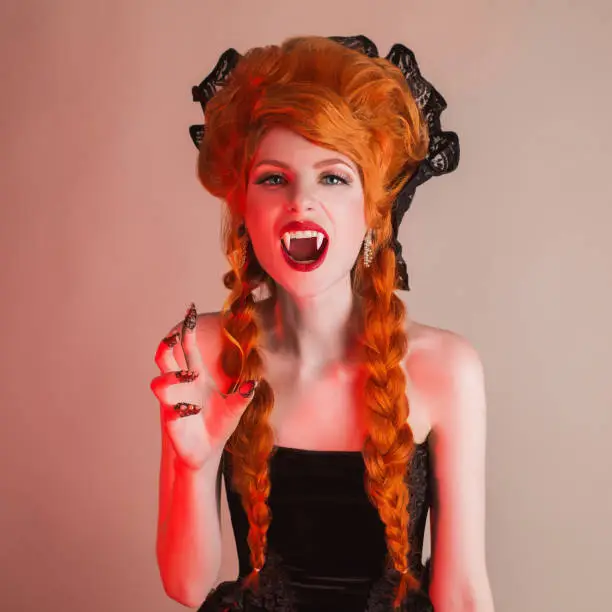 Gothic halloween clothes. Young terrible redhead queen with hairstyle. Demon with red hair. Vampire with sharp fangs. Terrible outfit for halloween party. Undead demon vampire in gothic dress.