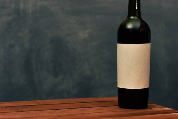 istock Red wine bottle with a white textural label on an old wooden table. Beautiful dark background 1053801100