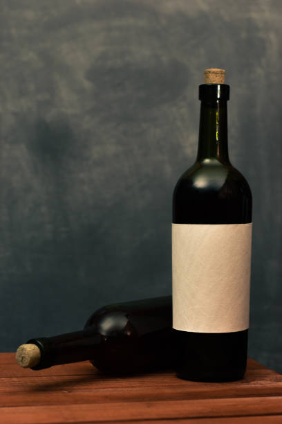 istock Red wine bottle with a white textural label on an old wooden table. Beautiful dark background 1053803144