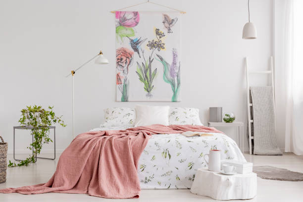 Peach blanket and white with green pattern linen on bed in a natural bright bedroom interior. Tapestry with colorful flowers and birds on the back wall. Real photo. Peach blanket and white with green pattern linen on bed in a natural bright bedroom interior. Tapestry with colorful flowers and birds on the back wall. Real photo. tapestry photos stock pictures, royalty-free photos & images
